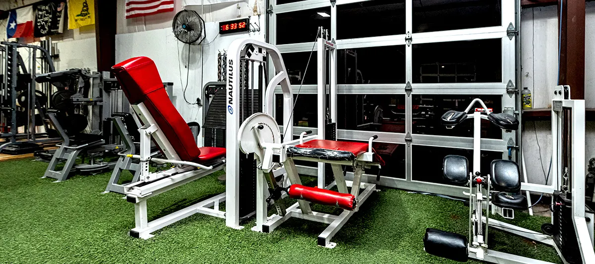 The machine floor: rows of plate-loaded and selectorised machines on turf, with a roll-up door letting in daylight behind them.